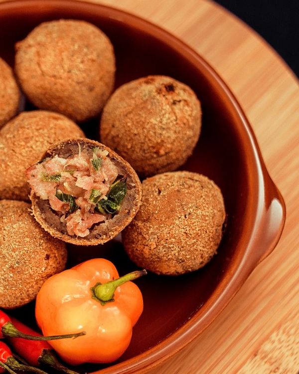 Bolinhos de feijoada numa cumbuca de barro, um deles aberto mostrando o recheio, com pimentas