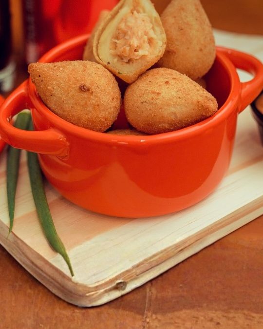 Coxinhas de frango fritas numa panelinha laranja, uma delas aberta mostrando o recheio