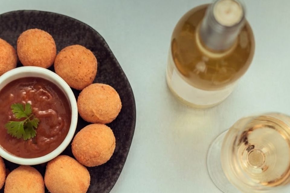 Vista de cima de um prato de bolinhos com molho, uma garrafa e uma taça de vinho branco