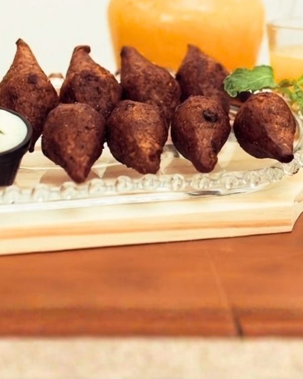 Quibes de carne fritos numa travessa de vidro, com molho branco e suco ao fundo