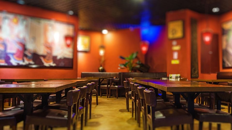 Salão de restaurante com mesas de madeira e paredes laranja