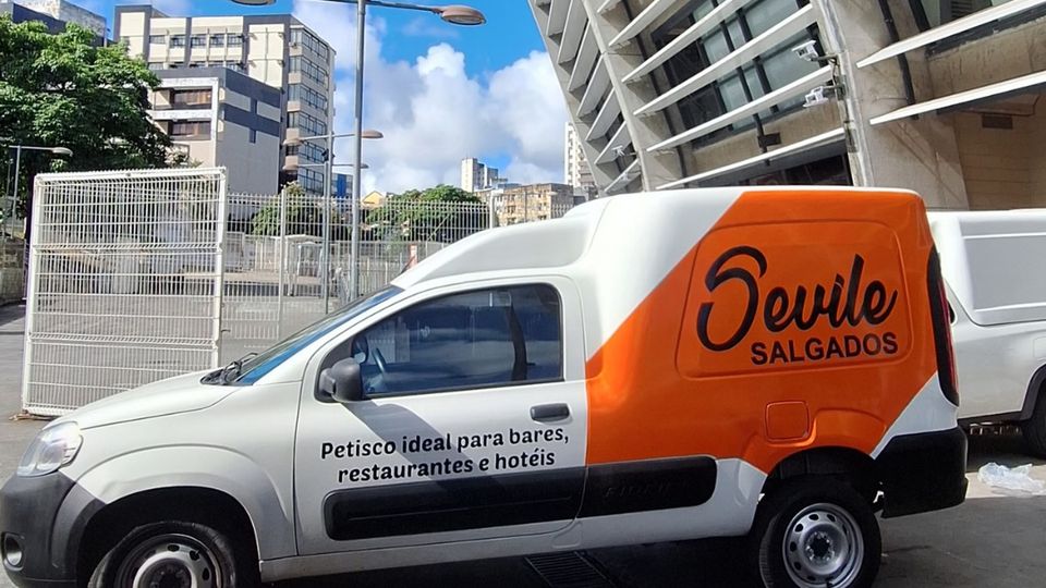 Furgão branco e laranja com a marca Sevile Salgados pintada na lateral
